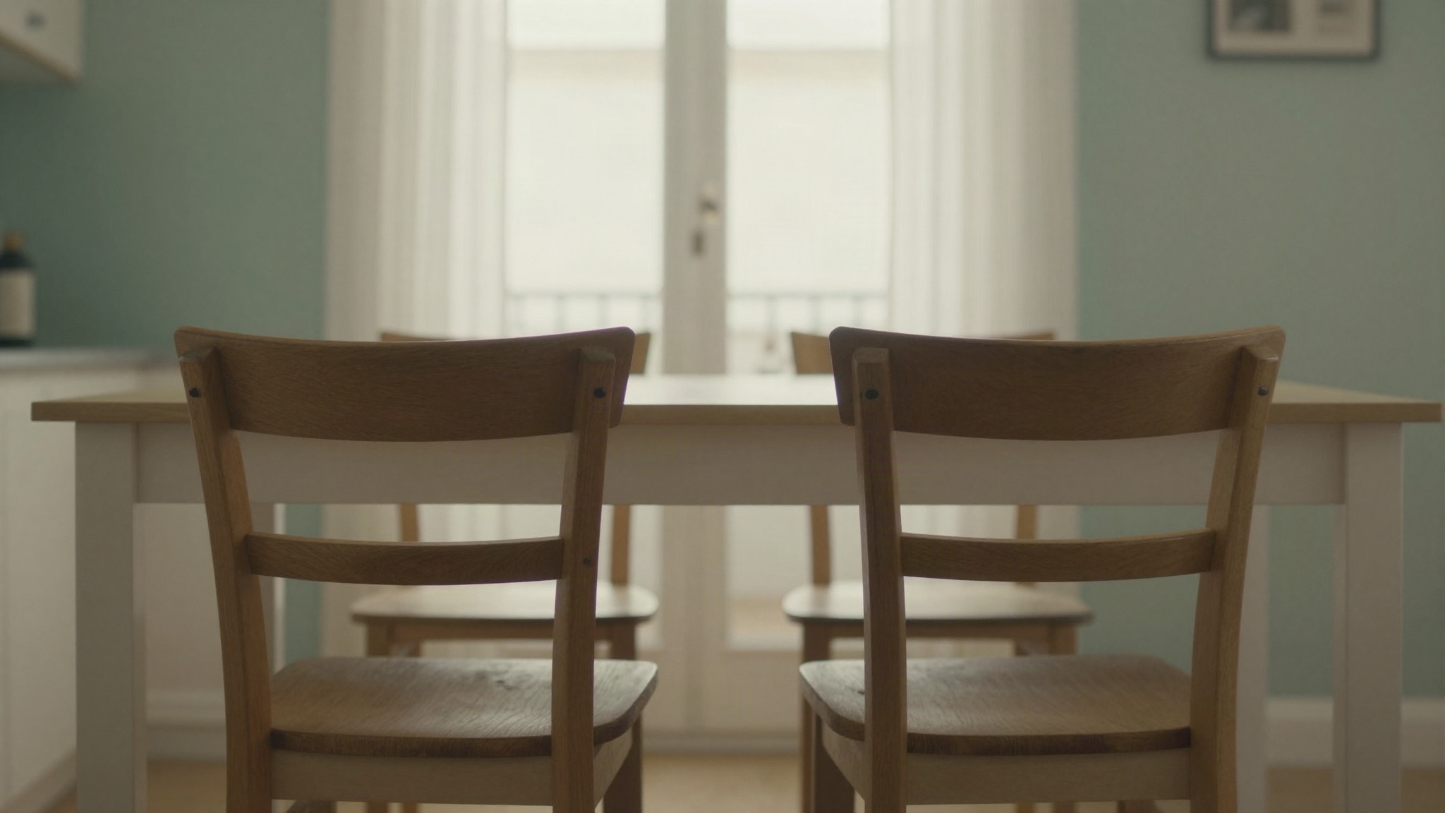 Dos sillas de madera juntas a una mesa de cocina, una ligeramente apartada
